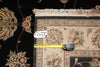 Load image into Gallery viewer, A close-up of a patterned area rug with cream fringe, shown alongside a yellow tape measure and a small white tag with product code 'Doc-12946 5.9x8.