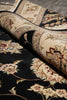 Load image into Gallery viewer, A close-up of a traditional oriental-style rug with a black base and beige floral motifs, partially rolled to show the pattern and texture.