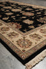 Load image into Gallery viewer, A traditional oriental area rug with a black field, beige borders, and floral motifs in cream, rust, and green, shown on a gray tiled floor.