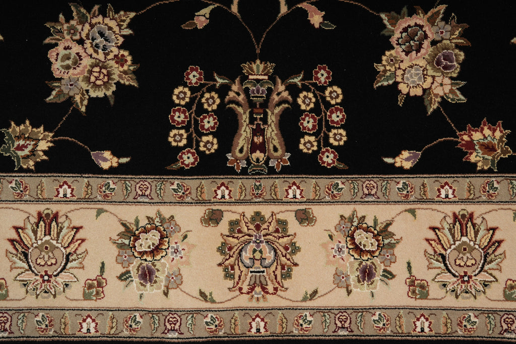 Close-up of an ornate floral rug pattern with a black upper field, a beige decorative border, and multicolored motifs including flowers, leaves, and central medallions.