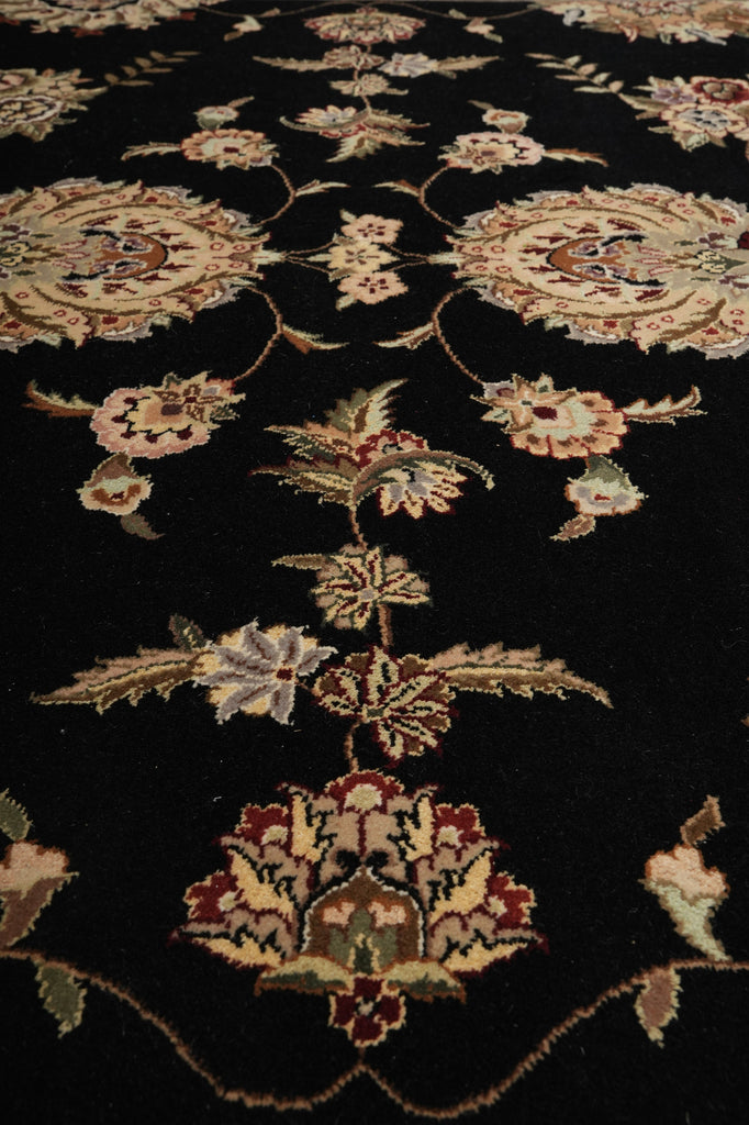 Close-up of a traditional oriental rug with a black background and ornate floral motifs in beige, muted green, and burgundy.