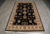 Load image into Gallery viewer, A rectangular area rug with a black center field and beige floral motifs, laid out on a gray wood-look floor.