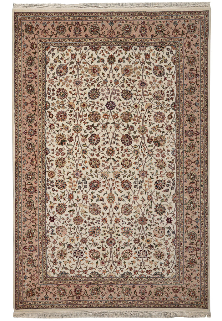 A traditional rectangular area rug with an intricate floral and vine pattern, featuring a beige and cream center field, a dusty rose border, and fringed edges.