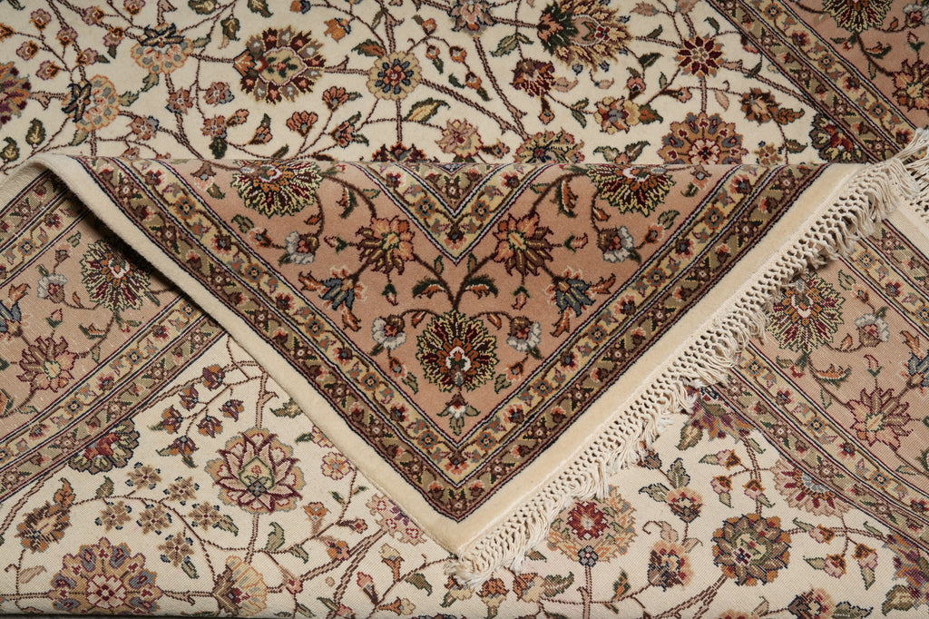 A close-up of an ornate Persian-style area rug with a floral pattern, featuring a central dusty pink triangular panel, cream borders, and white fringe.
