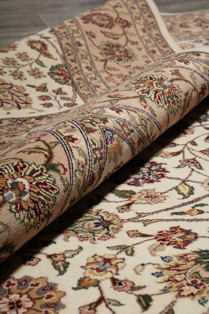A close-up of a rolled area rug showing its detailed floral and vine pattern in beige, cream, brown, and muted red tones.