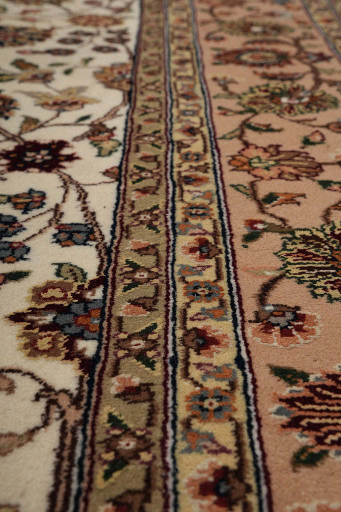 Close-up of an ornate patterned area rug showing floral motifs and detailed borders in beige, cream, pink, green, blue, and brown tones.