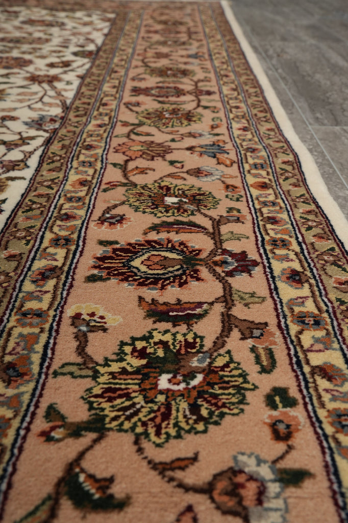 A close-up view of a traditional oriental runner rug with a floral pattern on a warm beige background, laid out on a gray tiled floor.