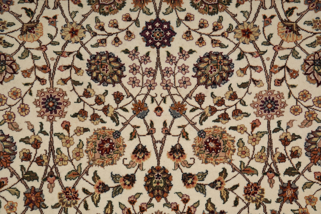A close-up of an ornate floral patterned rug with cream, beige, brown, and muted pink tones, featuring intricate traditional motifs and vines filling the frame.