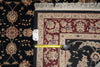 Load image into Gallery viewer, A close-up of a patterned area rug corner with a yellow tape measure laid across it to show dimensions. The rug has a dark navy or black field with beige floral motifs and a burgundy border section.