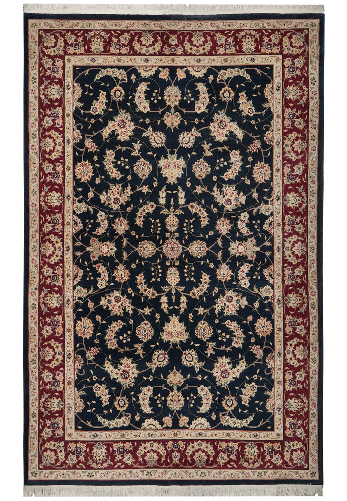 A traditional oriental area rug with an intricate floral pattern, featuring a dark navy blue center field, a deep red border, and cream-colored details, shown flat against a white background.