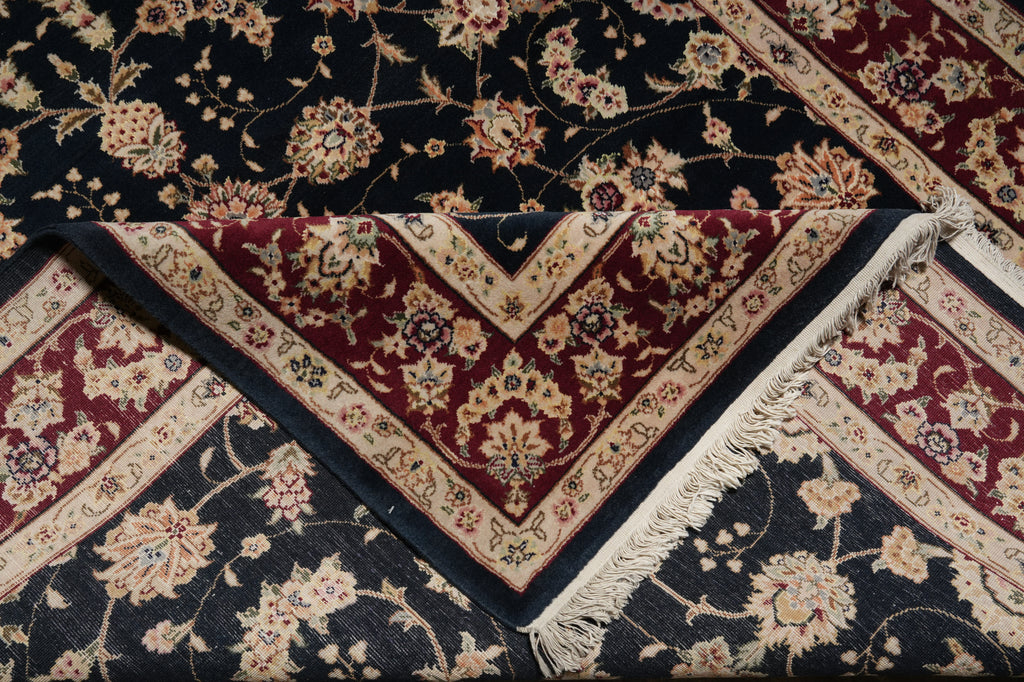 A folded traditional oriental rug with a dark navy blue field, deep red borders, and cream floral motifs, shown with fringe visible on one corner.