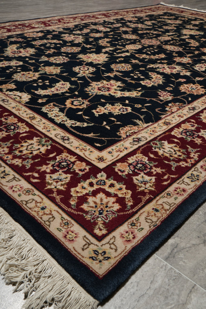 A traditional oriental area rug with a dark navy blue field, a deep red border, and cream floral motifs, shown on a light gray tiled floor.