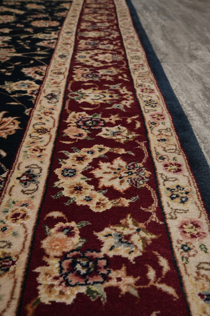 A close-up view of a traditional patterned runner rug with a deep red center, cream floral motifs, and blue accents, laid out on a gray floor.