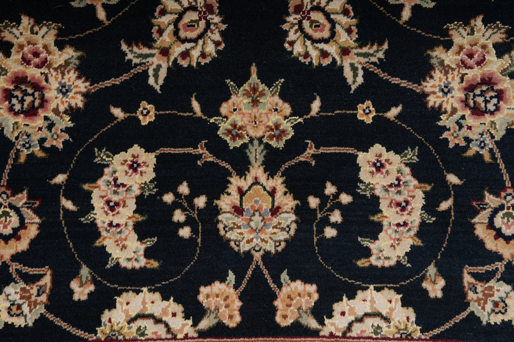 A close-up of a traditional floral patterned rug with cream, beige, and muted red flowers on a very dark navy or near-black background.