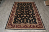 Load image into Gallery viewer, A rectangular traditional area rug with a dark navy blue center, red and beige floral borders, and white fringe, laid out on a gray wood-look floor.