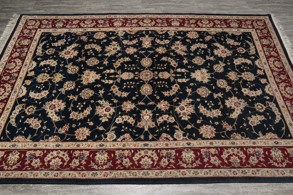 A traditional oriental area rug with a black field, red borders, and beige floral motifs, shown flat on a gray tiled floor.