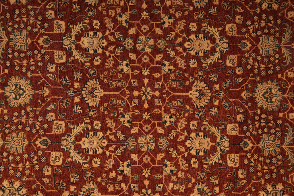 A close-up of an ornate traditional rug with a deep red-brown field, beige floral medallions, and dark blue accents in a repeating geometric and floral pattern.
