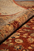 Load image into Gallery viewer, A close-up of a traditional patterned area rug with one end rolled back to show the pile and reverse side, featuring warm rust red, beige, and dark navy floral motifs.
