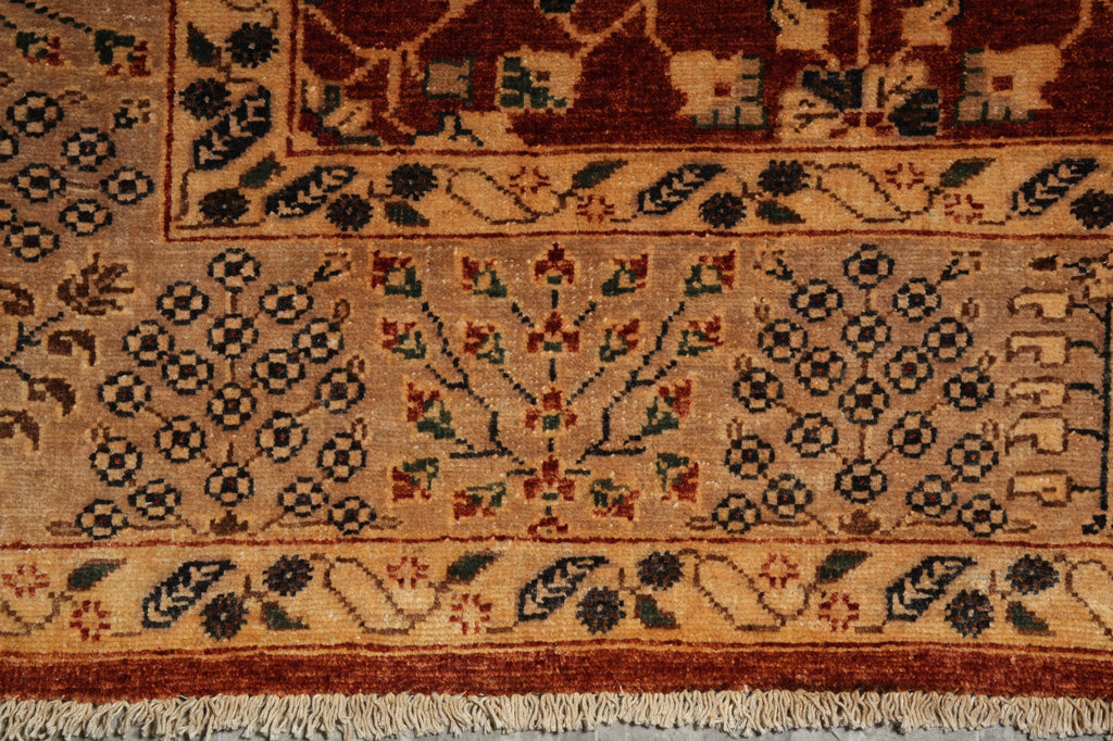 Close-up of a patterned rug showing a beige field with dark brown floral motifs, a central red and green tree-like medallion, and a decorative border with cream fringe.