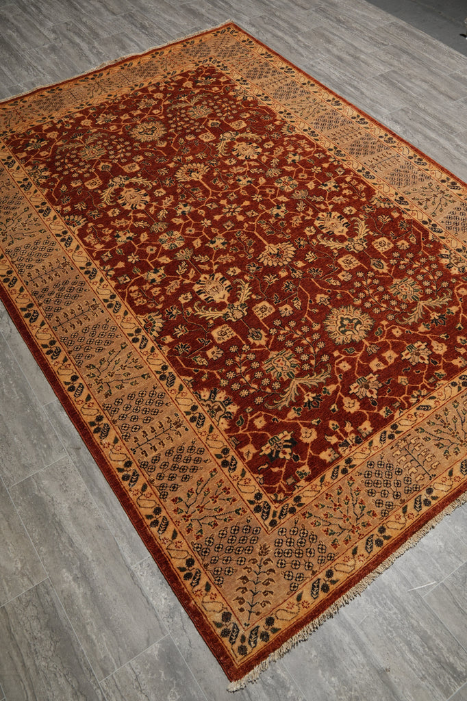 A traditional oriental area rug with a deep red central field, beige and gold floral motifs, and a patterned border, shown laid out on a gray wood floor.