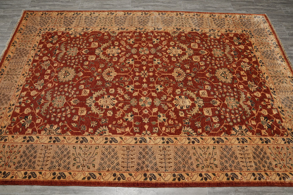 A rectangular traditional area rug with an intricate floral and geometric pattern, featuring a deep red center field and beige borders, laid out on a gray wood floor.