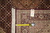 Load image into Gallery viewer, A close-up of an ornate patterned area rug corner with a yellow tape measure and a small handwritten size tag placed on it, showing the rug's pattern and fringe detail.