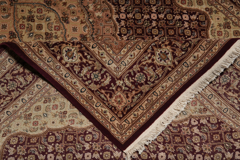 A close-up of an ornate patterned area rug with cream, burgundy, and brown tones, showing detailed floral motifs and white fringe along one corner.