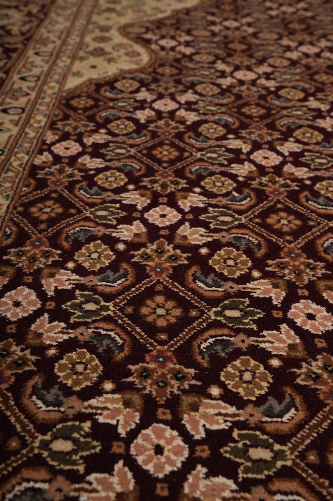 A close-up view of an ornate traditional rug with a dark brown base and intricate floral and geometric patterns in beige, brown, muted green, and cream.