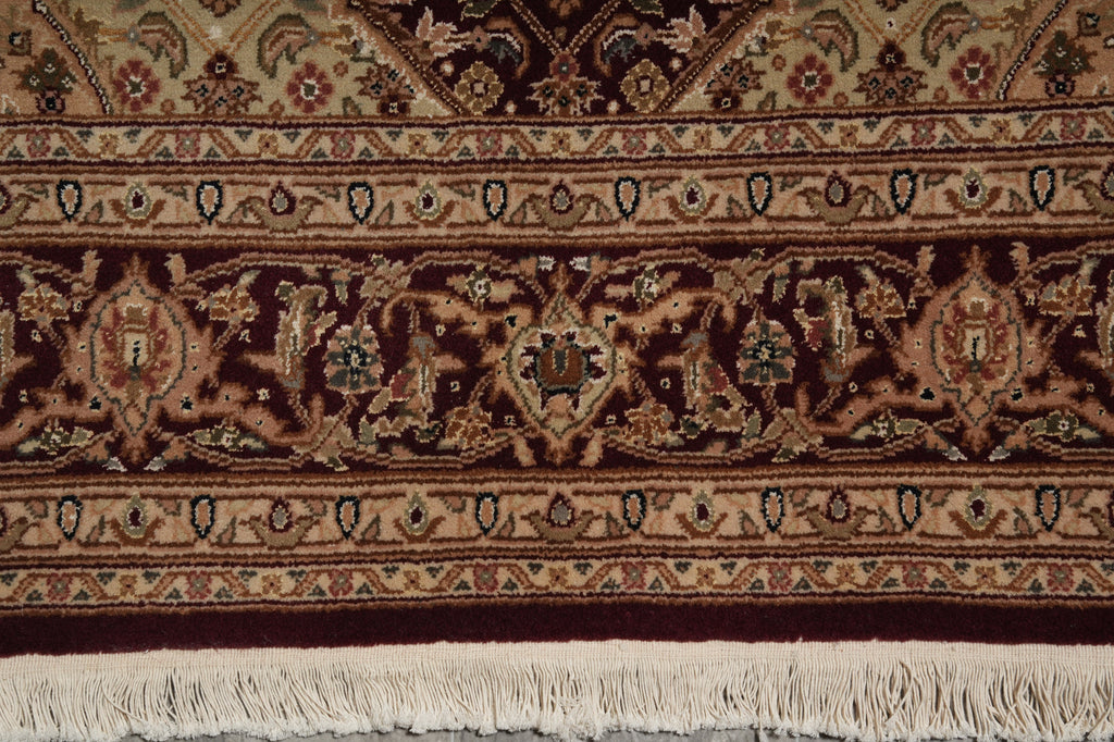 A close-up of an ornate patterned rug with cream fringe, featuring dark brown, burgundy, beige, and muted blue floral and geometric motifs.