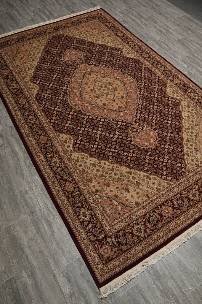 A traditional oriental-style area rug with an intricate floral and geometric pattern in shades of brown, beige, and burgundy, shown laid out on a gray wood-look floor.