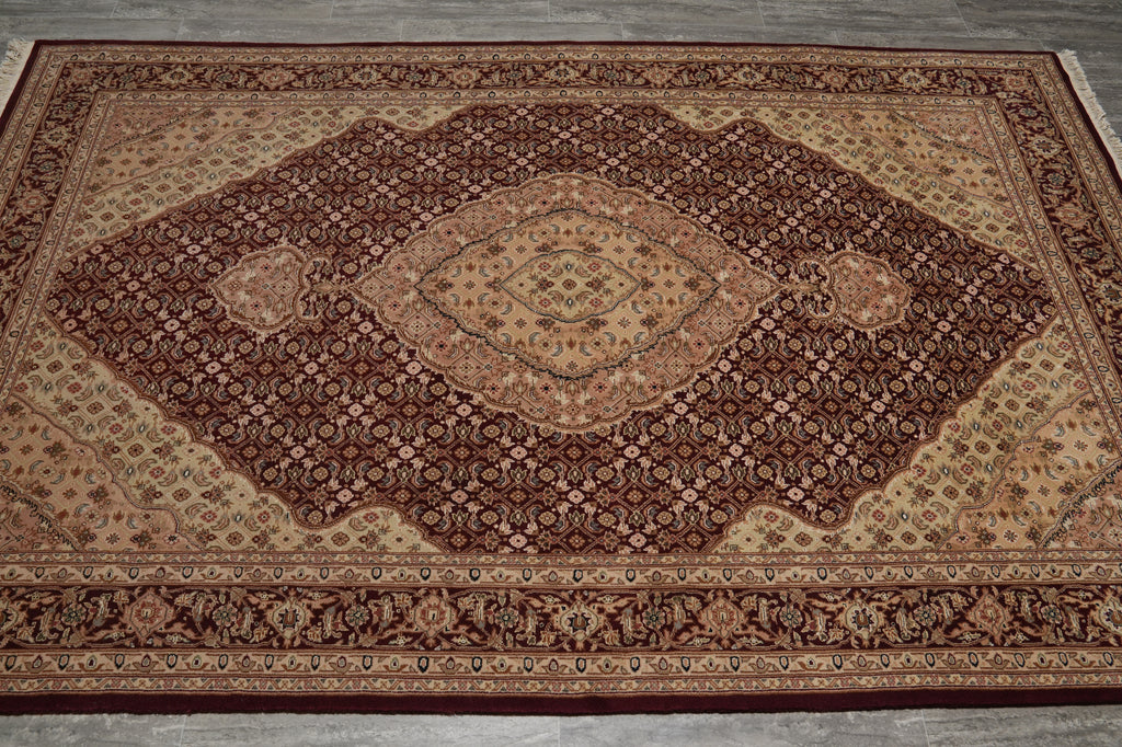 A traditional oriental area rug with an intricate floral pattern, featuring a large central diamond medallion in shades of dark brown, rust red, and beige, laid out on a gray concrete floor.