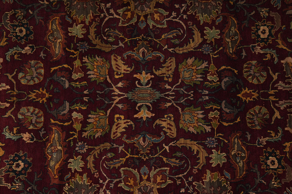 A close-up of an ornate traditional rug with a deep burgundy background and intricate floral and vine motifs in muted gold, olive green, and blue.