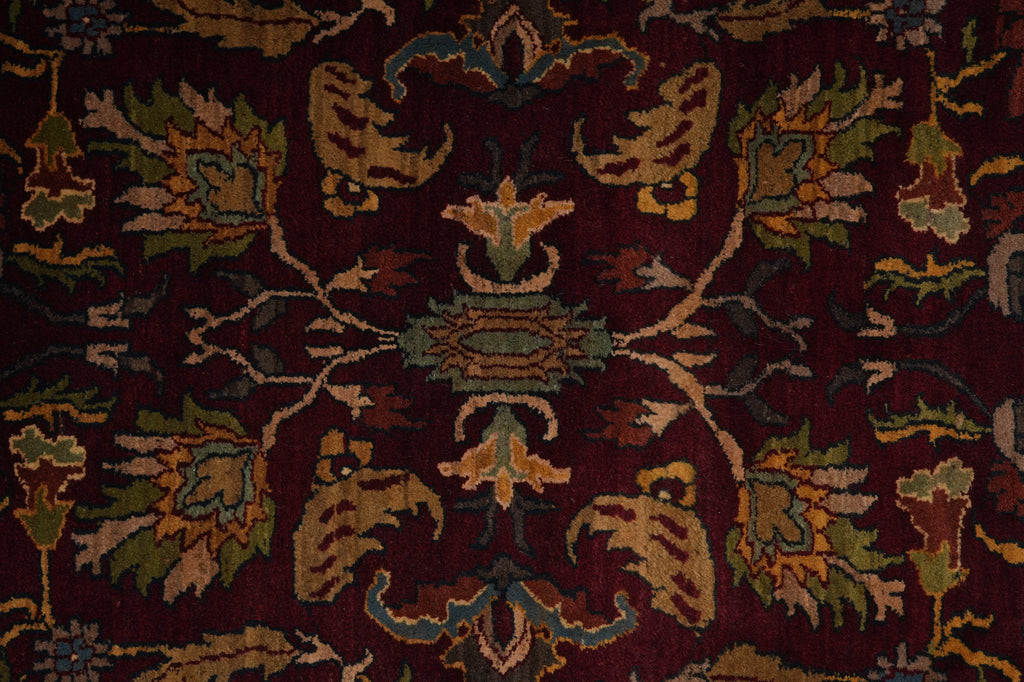 A close-up of an ornate traditional rug featuring a deep burgundy background with intricate floral and vine motifs in muted green, beige, and gold tones.