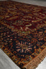 Load image into Gallery viewer, A close-up of a traditional oriental rug with a dark red field, a dark navy blue border, and intricate floral motifs in beige, gold, and green, finished with a fringed edge.