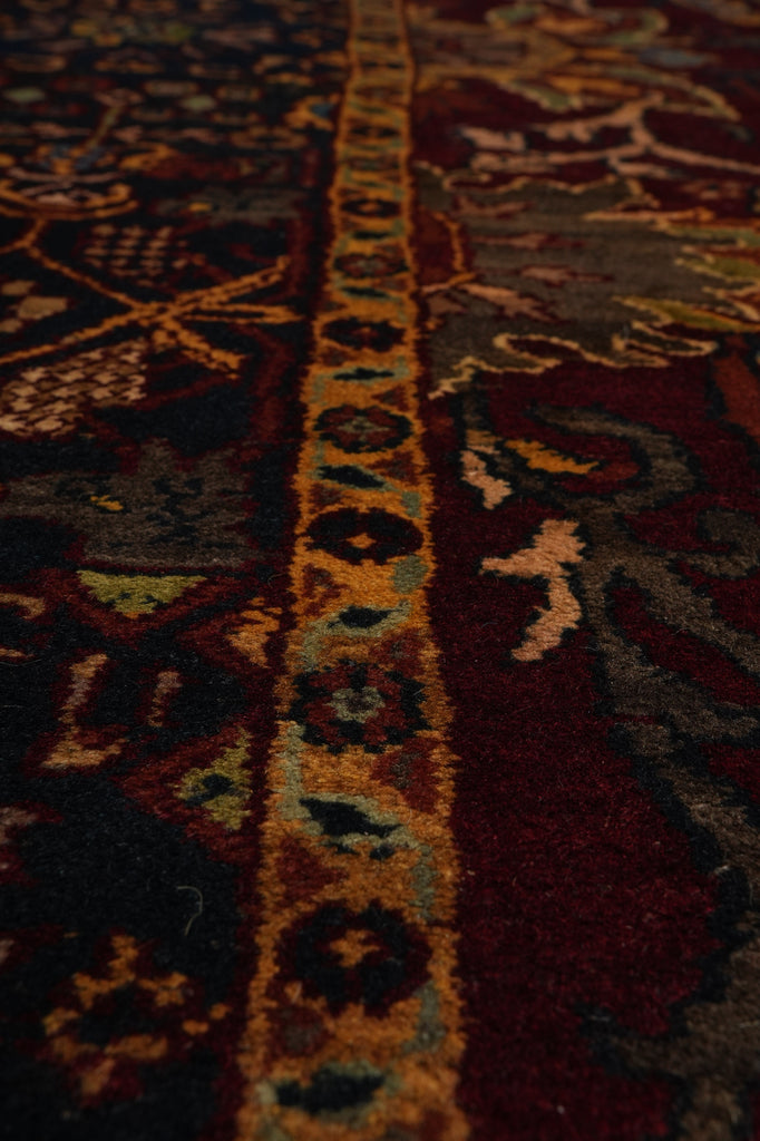 Close-up of a traditional patterned rug with a central ornamental border in gold, beige, and teal, surrounded by deep red and dark brown sections.