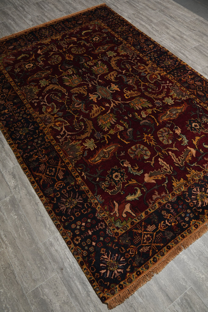 A traditional oriental area rug with an intricate floral and animal pattern, shown laid out on a gray wood-look floor. The rug features a deep burgundy center, dark navy borders, and warm brown and gold accents.