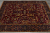 Load image into Gallery viewer, An antique Persian-style area rug with a deep red central field, intricate floral and bird motifs, and dark navy blue borders with gold detailing, laid out on a gray floor.
