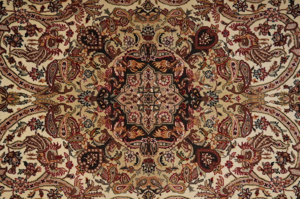 A close-up of an ornate traditional patterned rug with a central medallion and symmetrical floral motifs in beige, rust red, brown, and black.