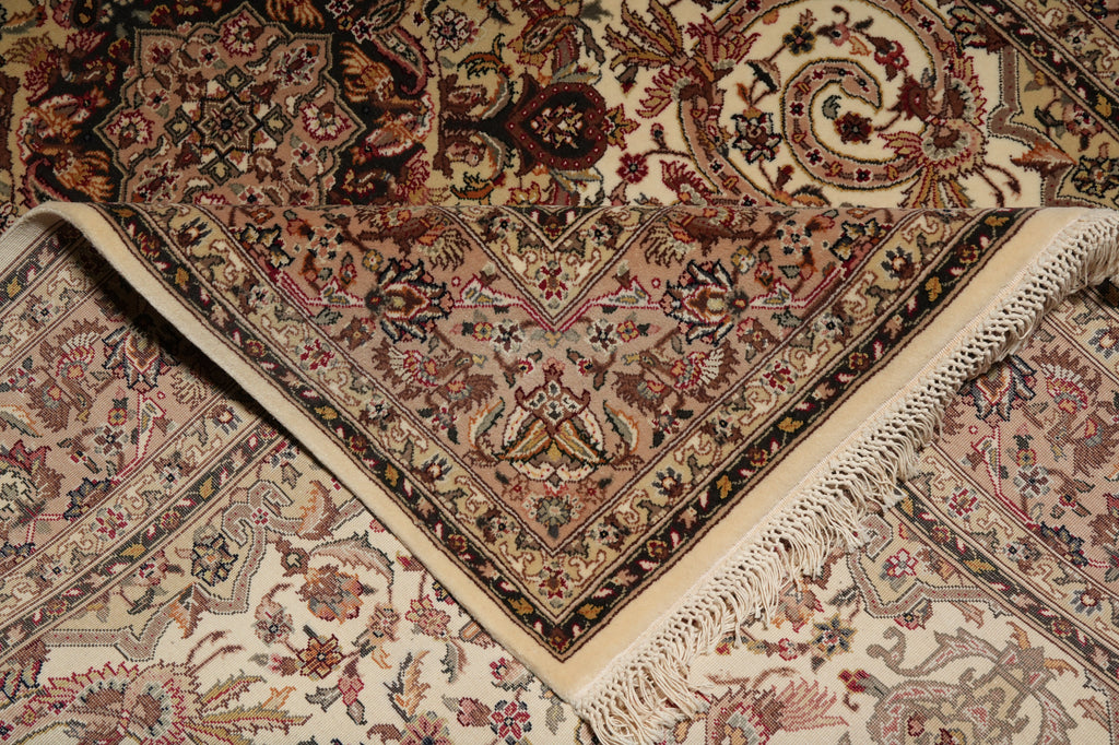 A close-up of a traditional oriental rug with an intricate floral and geometric pattern in beige, brown, and muted red tones, showing folded corners and cream fringe.