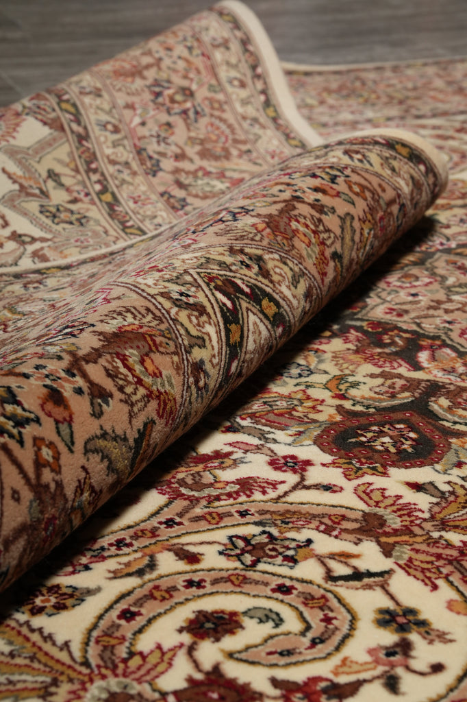 A close-up of a rolled section of a traditional oriental rug showing its detailed floral and scroll patterns in beige, red, brown, and cream tones.
