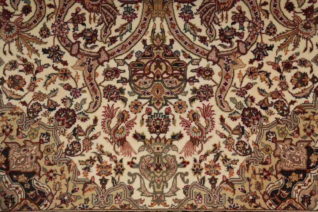 A close-up of an ornate traditional patterned rug with a cream background and intricate floral, bird, and scroll motifs in muted red, brown, green, and black tones.
