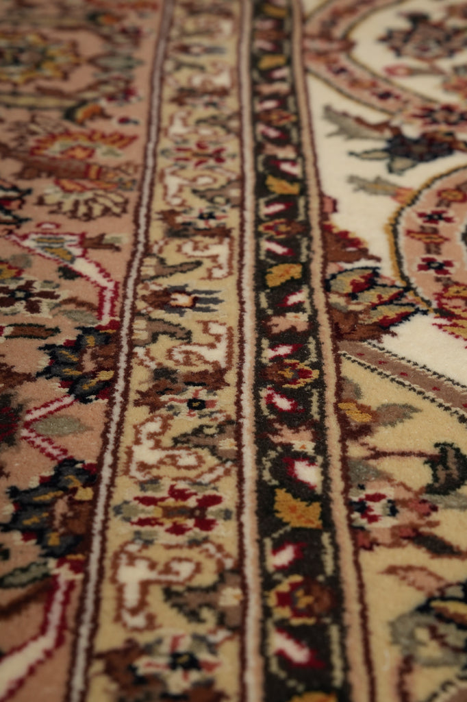 Close-up of an ornate patterned area rug with beige, cream, red, brown, and green tones, showing detailed woven borders and floral motifs.