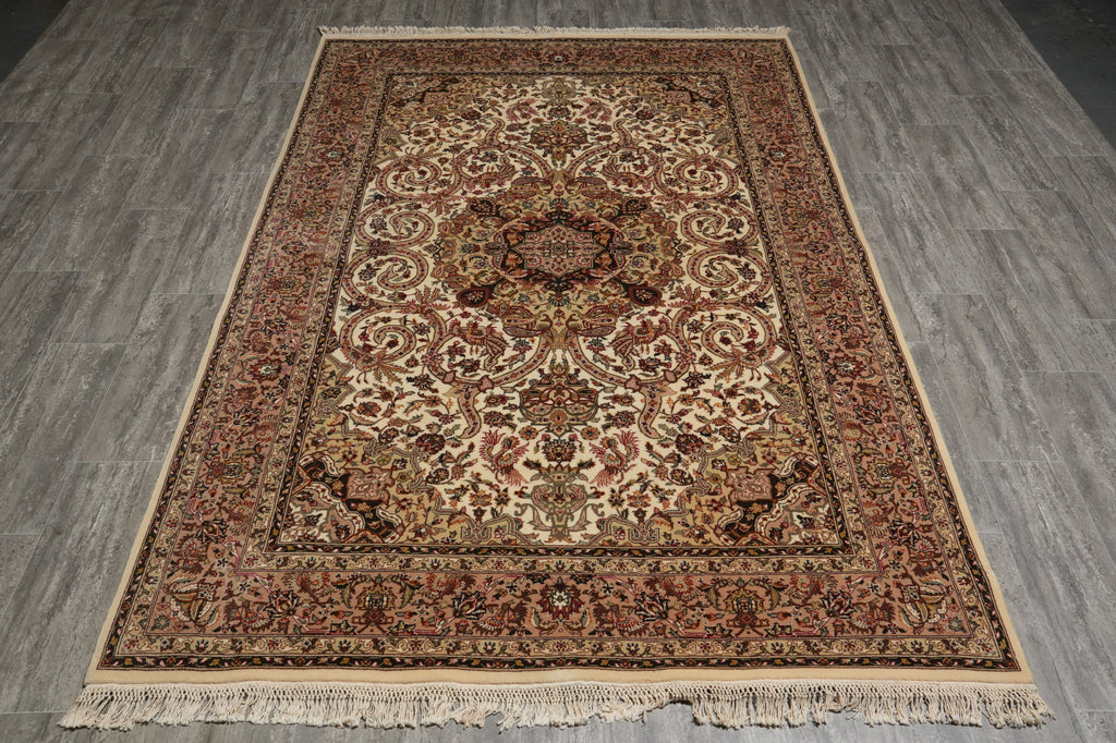 A traditional oriental-style area rug with an intricate floral and medallion pattern, laid flat on a gray wood-look floor. The rug features a warm brown, beige, and red color palette with cream-colored fringe at the bottom.
