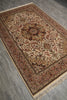 Load image into Gallery viewer, An ornate rectangular area rug with a traditional medallion and floral pattern, shown from an elevated angle on a gray wood-look floor. The rug features a cream center, a warm brown border, and beige fringe.