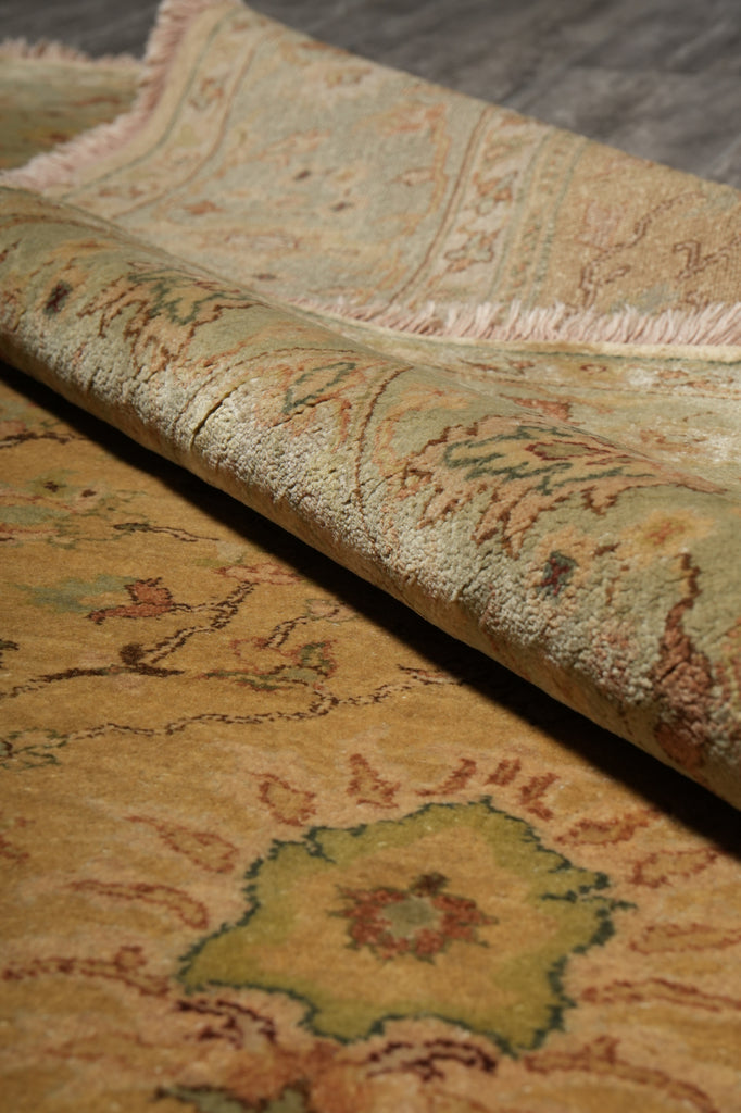 A close-up of a rolled area rug showing its detailed floral pattern in muted tones of beige, sage green, and terracotta.