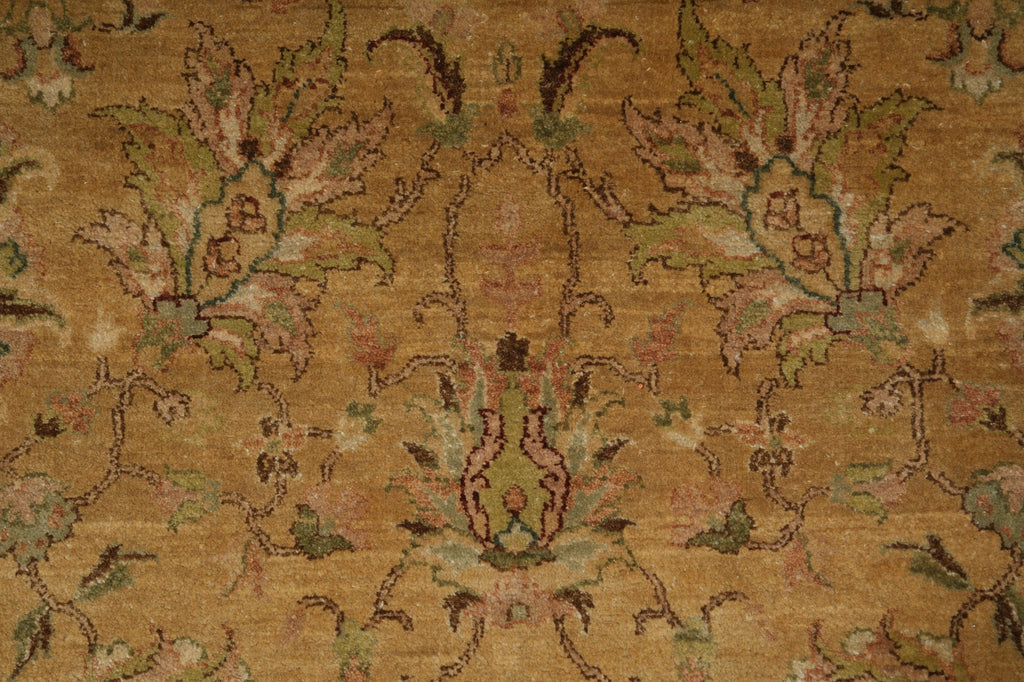 A close-up of an ornate floral patterned rug in warm tan and beige tones with muted green, pink, and brown detailing.
