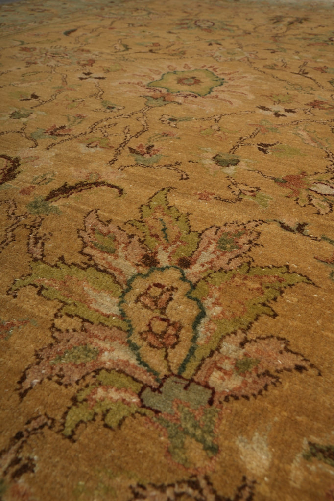 A close-up view of a traditional patterned area rug with a warm tan and beige base, featuring large floral motifs in muted green, brown, and soft pink.