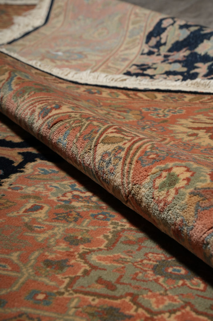 A close-up of a folded area rug showing its detailed traditional pattern in muted tones of rust, beige, blue, and green.