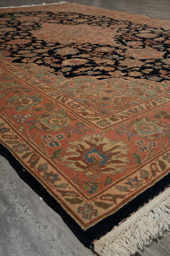 A traditional oriental-style area rug with a terracotta orange field, black border, and cream fringe, photographed on a gray concrete floor.