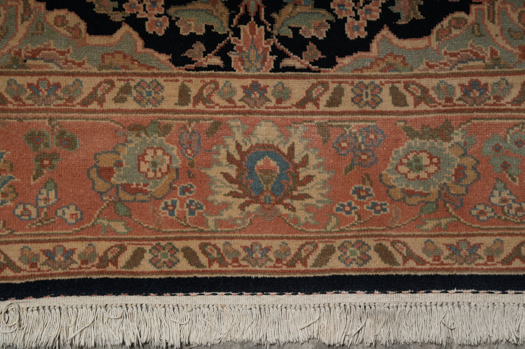 Close-up of an ornate patterned rug showing a terracotta field, cream and blue floral motifs, a dark navy border, and white fringe tassels.